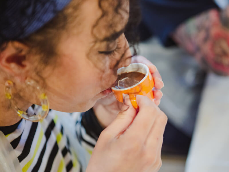 A woman sips chocolate from a small orange mug